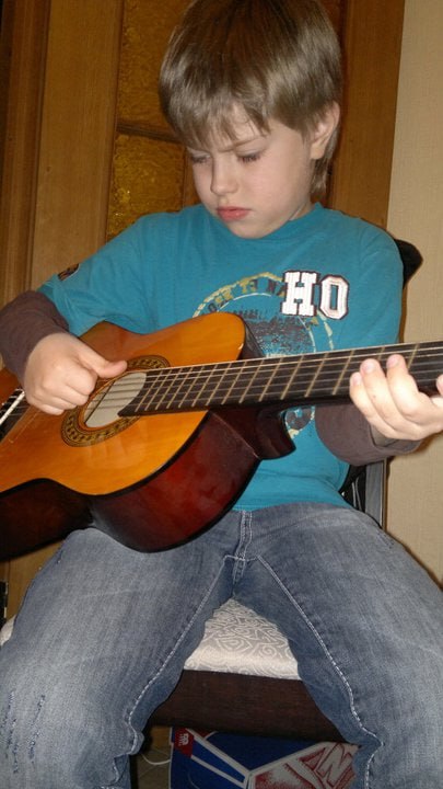 A young boy playing a classical guitar, concentrating on his left hand